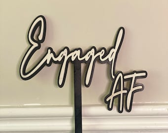 May include: White cursive text on a black background reads "Engaged AF" with a black stick attached to the bottom.