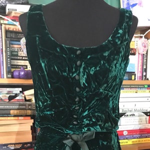 May include: A sleeveless emerald green velvet dress with a bow at the waist and a row of buttons down the front.