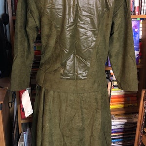 May include: A green suede dress with a leather panel on the back. The dress has a long skirt and long sleeves.