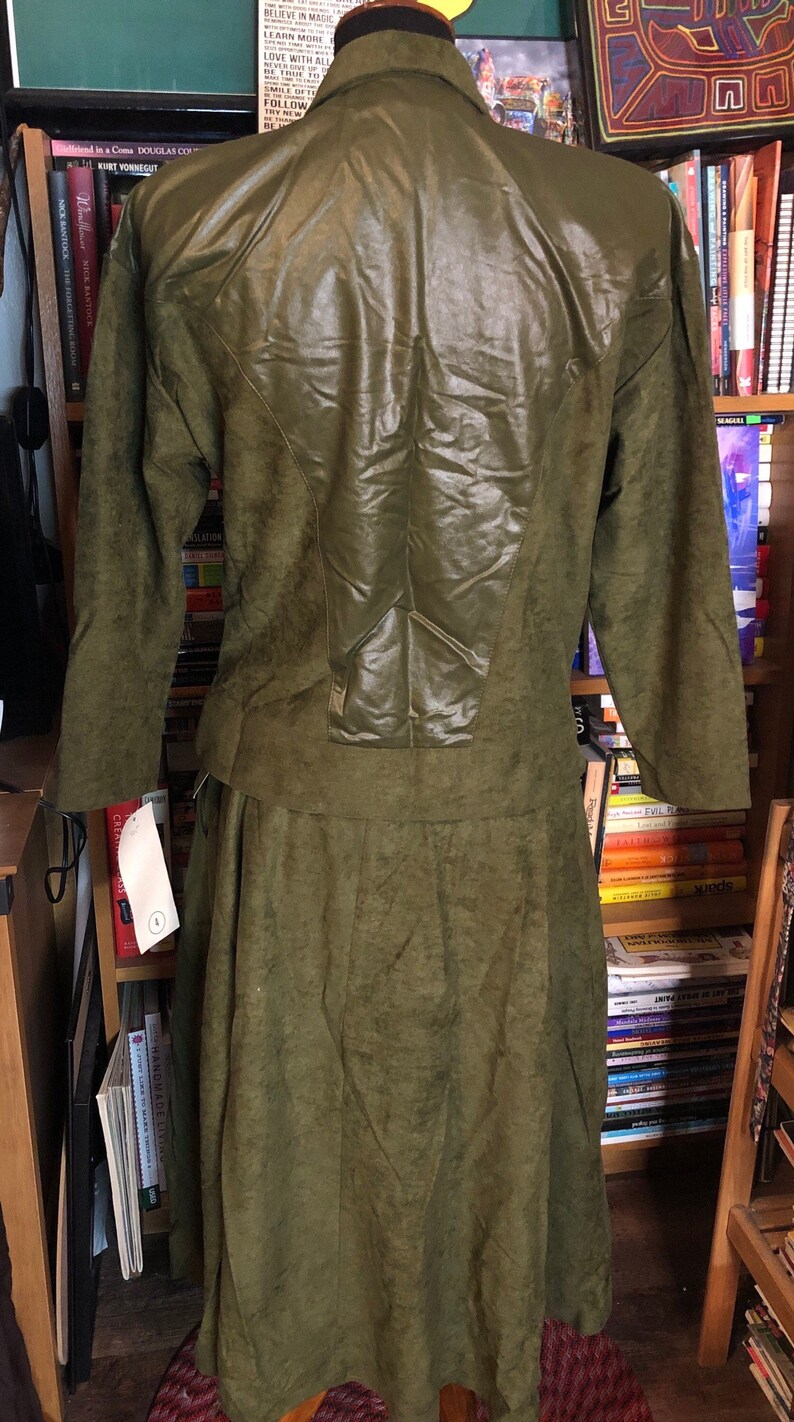 May include: A green suede dress with a leather panel on the back. The dress has a long skirt and long sleeves.