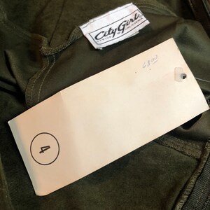 May include: A white tag with the text "City Girl Styled in California" and the number "4" circled. The tag is attached to a dark green garment.