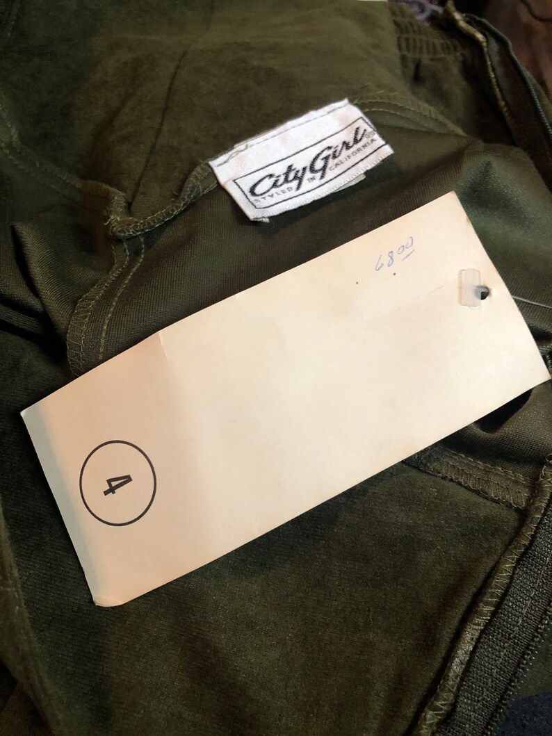 May include: A white tag with the text "City Girl Styled in California" and the number "4" circled. The tag is attached to a dark green garment.
