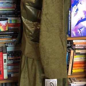 May include: A green, long-sleeved jacket with a matching skirt. The jacket has a shiny, almost metallic, finish. The skirt is a more matte fabric. The outfit is displayed on a mannequin in front of a bookshelf. A tag with the text "City Girl" is attached to the skirt.