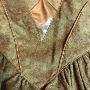 May include: A green velvet jacket with a gold diamond-shaped patch on the back. The jacket has a V-neck and is trimmed with brown cord.