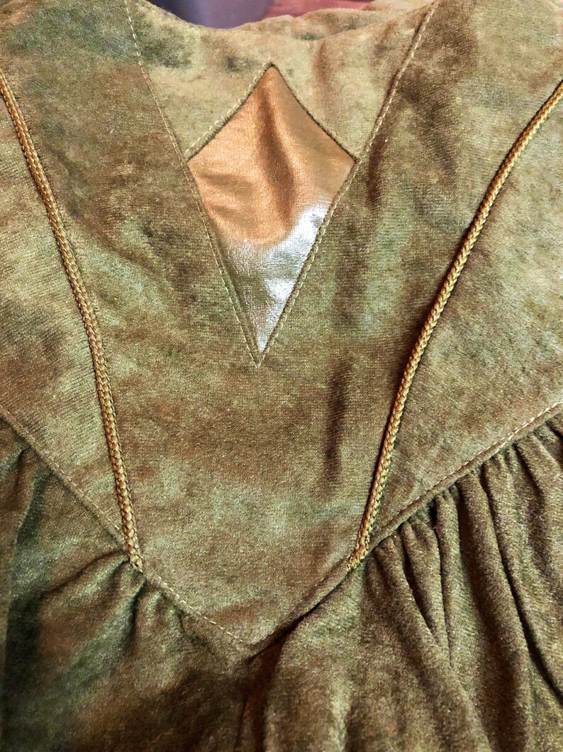 May include: A green velvet jacket with a gold diamond-shaped patch on the back. The jacket has a V-neck and is trimmed with brown cord.