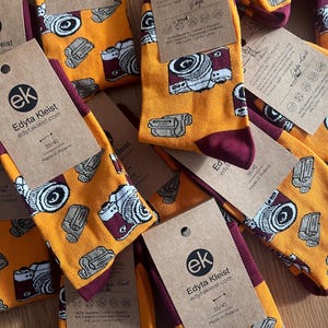 Op de afbeelding: Een set gele en kastanjebruine sokken met een camera-ontwerp. De sokken zijn gemaakt in Polen en zijn maat 35/40. De sokken zijn gemaakt van 80% katoen, 10% polyester, 4% Lycra en 6% polyamide.