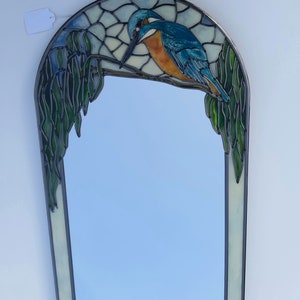 Pode incluir: Um espelho de vidro colorido com um guarda-rios azul e laranja empoleirado em um galho com folhas verdes. O espelho tem uma borda branca e um fundo azul claro.