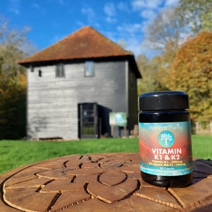 May include: A black plastic bottle of Ancient Purity Vitamin K1 & K2 dietary supplement capsules. The label features a gradient background, a tree logo, and text stating Vitamin K1 - 300mcg and K2 (Natto MK-7) - 150mcg with 90 capsules total.