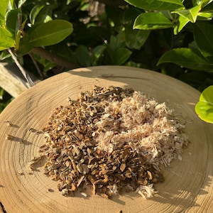 Peut inclure: Une tranche de bois présente deux tas de matières naturelles. L'un est composé de petits morceaux brun foncé, l'autre d'une texture déchiquetée beige clair. Le fond est composé de feuillage vert.