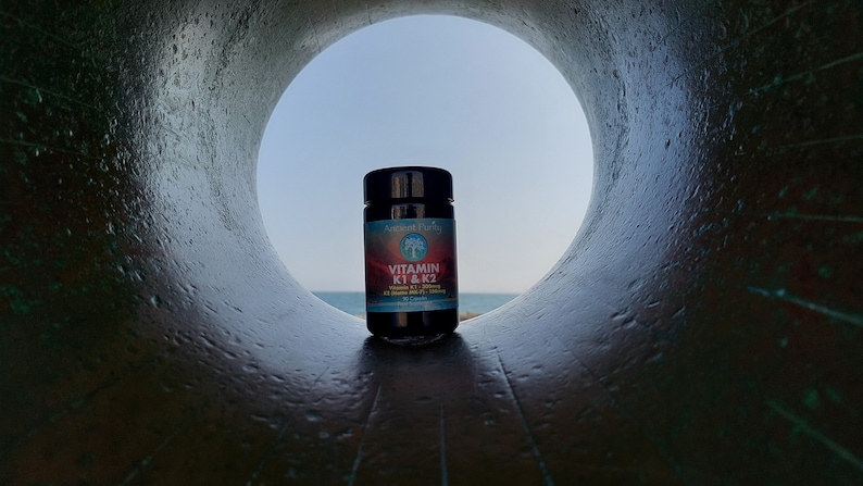 May include: A dark-colored supplement bottle with a black cap and a label featuring a tree logo, the text Vitamin K1 & K2, and additional supplement details. The bottle is positioned within a circular opening that frames the product against a sky.