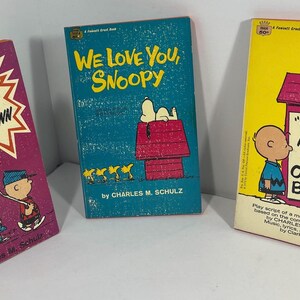 May include: Three vintage Peanuts comic book play scripts. The first is pink with the text "You're a Brave Man Charlie Brown". The second is blue with the text "We Love You, Snoopy" and the third is yellow with the text "You're a Good Man, Charlie Brown".