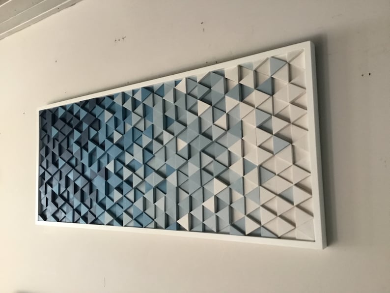 Peut inclure: Une &oelig;uvre d'art murale en bois avec un d&eacute;grad&eacute; de triangles bleus. Les triangles sont dispos&eacute;s en un motif g&eacute;om&eacute;trique et sont peints dans des nuances de bleu, du bleu fonc&eacute; au bleu clair. La pi&egrave;ce est encadr&eacute;e de blanc.