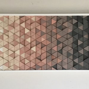 May include: A framed wall art piece made of wood triangles in shades of white, pink, and gray. The triangles are arranged in a gradient pattern, transitioning from light to dark.