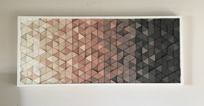 May include: A framed wall art piece made of wood triangles in shades of white, pink, and gray. The triangles are arranged in a gradient pattern, transitioning from light to dark.