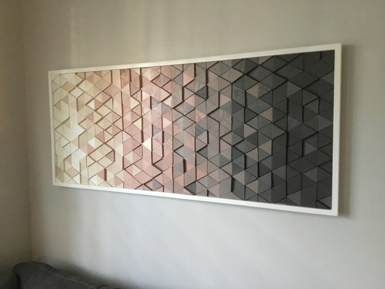 May include: A framed wall art piece made of wood triangles in shades of beige, pink, brown, and gray. The triangles are arranged in a geometric pattern, creating a gradient effect.