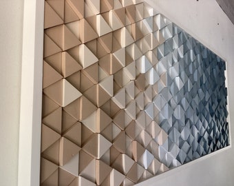 May include: A wall art piece made of a geometric pattern of triangles in shades of beige, white, and blue. The triangles are arranged in a gradient pattern, starting with beige at the top and transitioning to blue at the bottom.