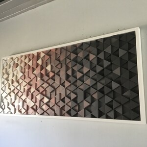May include: A framed wall art piece made of wood triangles in shades of beige, brown, and black. The triangles are arranged in a geometric pattern, creating a gradient effect.