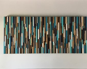 May include: A rectangular wooden wall art piece composed of vertical wooden slats in varying shades of blue, brown, and white. The artwork is mounted on a white wall, creating a striking contrast. The arrangement of the slats gives a textured, modern appearance.