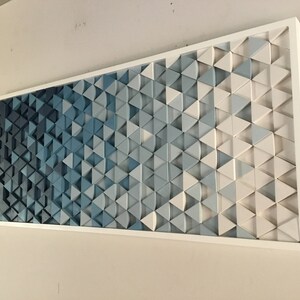 Peut inclure: Une &oelig;uvre d'art murale en bois compos&eacute;e de triangles de diff&eacute;rentes nuances de bleu et de blanc, dispos&eacute;s en d&eacute;grad&eacute;. Les triangles sont en 3D et cr&eacute;ent un effet textur&eacute;. L'&oelig;uvre est encadr&eacute;e d'un cadre blanc.
