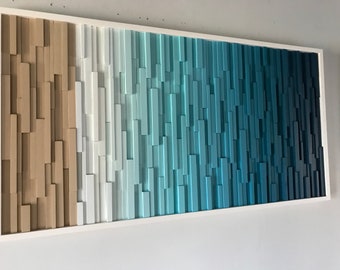 May include: A rectangular wooden wall art piece with a white frame. The artwork features vertical wooden blocks in shades of tan, white, and blue, creating an ombre effect. The blocks are arranged to give a 3D appearance.