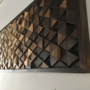 May include: A large wooden wall art piece with a geometric pattern of triangles in shades of brown. The piece is framed in a dark brown wood frame.