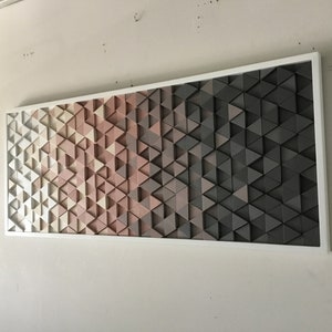 May include: A framed wall art piece featuring a geometric pattern of triangles in shades of white, pink, and gray. The triangles are arranged in a gradient pattern, with the white triangles at the top and the gray triangles at the bottom.