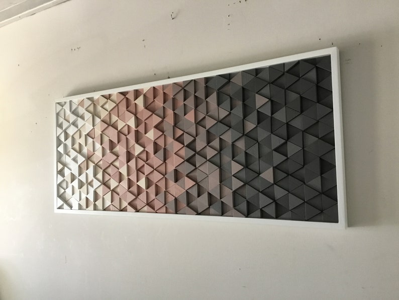 May include: A framed wall art piece featuring a geometric pattern of triangles in shades of white, pink, and gray. The triangles are arranged in a gradient pattern, with the white triangles at the top and the gray triangles at the bottom.