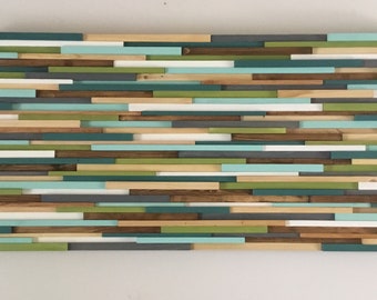May include: A wall art piece made of wood slats painted in shades of green, blue, gray, and white. The slats are arranged in a horizontal pattern, creating a modern and abstract design.