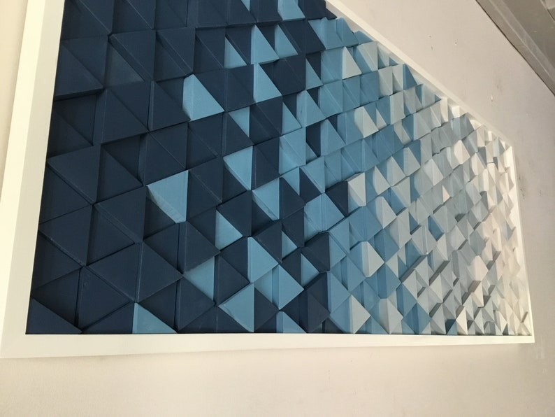 Peut inclure: Une &oelig;uvre d'art murale encadr&eacute;e pr&eacute;sentant un d&eacute;grad&eacute; de formes triangulaires bleues et blanches. Les triangles sont dispos&eacute;s en quinconce, cr&eacute;ant une impression de profondeur et de mouvement.