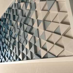 Peut inclure: Une &oelig;uvre d'art murale encadr&eacute;e compos&eacute;e de triangles en bois dans des tons de bleu et de blanc. Les triangles sont dispos&eacute;s selon un motif g&eacute;om&eacute;trique, cr&eacute;ant un effet de d&eacute;grad&eacute; du bleu fonc&eacute; au blanc.