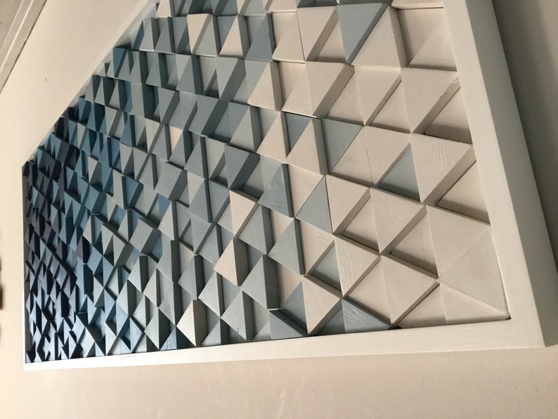 Peut inclure: Une &oelig;uvre d'art murale encadr&eacute;e compos&eacute;e de triangles en bois dans des tons de bleu et de blanc. Les triangles sont dispos&eacute;s selon un motif g&eacute;om&eacute;trique, cr&eacute;ant un effet de d&eacute;grad&eacute; du bleu fonc&eacute; au blanc.