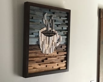 May include: A framed wood wall art piece with a coffee cup design. The cup is made of wood and has a brown, white, and gray color scheme. The background is a gradient of blue and brown wood.