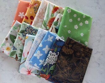 May include: A collection of 10 fabric squares with various floral and botanical patterns. The fabrics feature a variety of colors, including green, blue, black, white, and orange. The fabrics are arranged in a stack, with the top fabric being a dark green with white flowers.