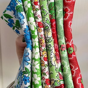 May include: A selection of floral fabric bundles in various colours. The fabrics display patterns of blue, green, red, and yellow flowers on a white background. The bundles are held together, displaying the range of designs.