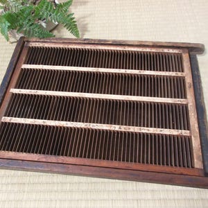 May include: A rectangular wooden frame with numerous vertical slats, creating a grid-like pattern. Three horizontal wooden supports are visible. The frame is a dark brown color, with some wear and tear visible. The item appears to be a vintage or antique piece.