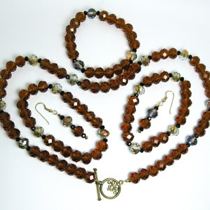 Peut inclure: Un ensemble de bijoux en perles de cristal brun et noir, comprenant un collier, un bracelet et des boucles d'oreilles. Le collier a un fermoir à glissière.
