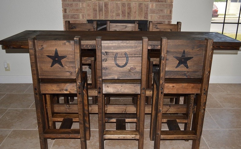 May include: A rustic wooden dining set with a table and six chairs. The chairs have a unique design with a star, horseshoe, or star on the back. The set is made of dark brown wood and has a distressed finish.