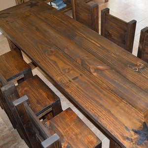 May include: A rustic wooden dining table with a dark brown finish and a star design. The table is surrounded by six matching chairs with a similar dark brown finish.