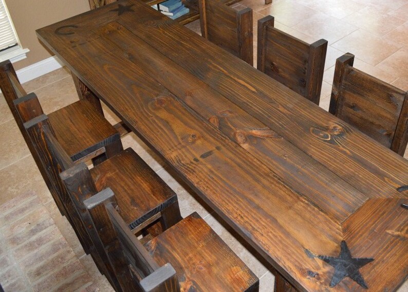 May include: A rustic wooden dining table with a dark brown finish and a star design. The table is surrounded by six matching chairs with a similar dark brown finish.