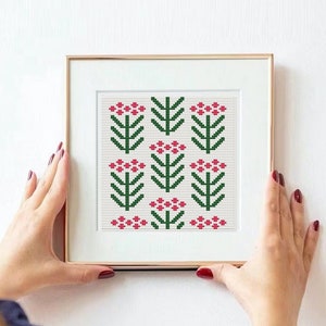 May include: A framed cross-stitch artwork featuring a repeating floral pattern. The design includes green stems and leaves with red flower clusters on a white background. The frame is gold-colored.