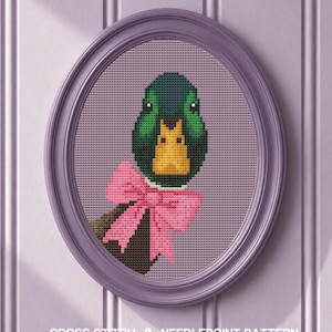 May include: An oval framed cross stitch embroidery featuring a mallard duck head with a dark green head, a bright yellow beak, and a large pink bow tied around its neck. The text CROSS STITCH & NEEDLEPOINT PATTERN is printed at the bottom.