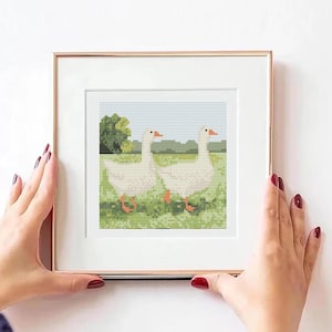 Puede incluir: Obra de punto de cruz enmarcada con dos gansos blancos caminando en un campo verde con un cielo azul y árboles en el fondo.