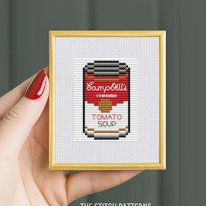 May include: A framed cross-stitch pattern of a red and white Campbell's Soup can with the text "Campbell's Condensed Tomato Soup".