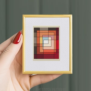 Puede incluir: Un patrón de punto de cruz enmarcado con un diseño geométrico de cuadrados concéntricos en tonos de rojo, naranja, amarillo y marrón.