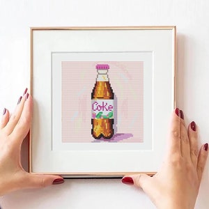 May include: A framed pixel art print of a brown glass bottle with a pink cap and a white label that says "Coke". The bottle is on a pink background with white dots.