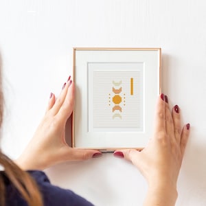 May include: A framed print featuring a geometric design in shades of orange, yellow, and white. The print is hung on a white wall.