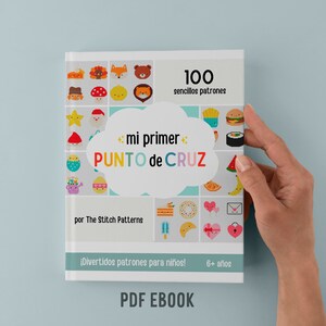 May include: A colorful book cover with the title "mi primer PUNTO de CRUZ" and the text "100 sencillos patrones" and "por The Stitch Patterns". The cover features a variety of colorful pixelated images, including animals, food, and hearts. The book is for children ages 6 and up.