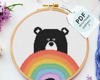 May include: A black bear cross stitch pattern with a rainbow. The pattern is in a hoop and there are four skeins of embroidery floss in the colors of the rainbow.