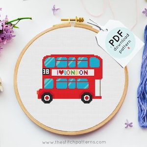 May include: A red double-decker bus with the words "I ♥ LONDON" on the side, in a wooden embroidery hoop. The bus is a cross-stitch pattern, and there are four skeins of embroidery floss in different colors next to the hoop.
