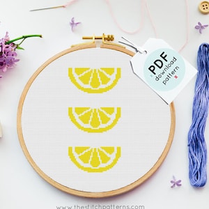 Puede incluir: Un patrón de punto de cruz de tres rodajas de limón amarillas en un aro de bordado de madera. El aro está sobre una superficie blanca con hilo de bordar, botones y una etiqueta que dice "Patrón de descarga PDF".